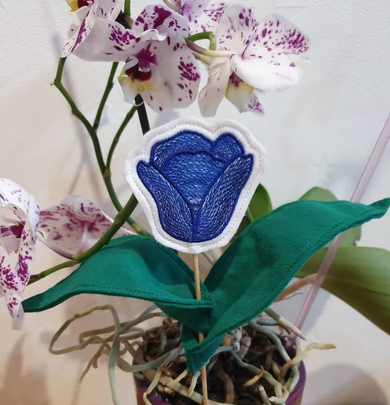Stickdatei ITH Tulpe (10x10 und größer), Foto zeigt in Orchideentopf eingesteckten Stab mit Tulpenkopfdesign in Blau auf weißem Untergrund. 2 Blätter, aus grünem Filz genäht, an Stab befestigt.