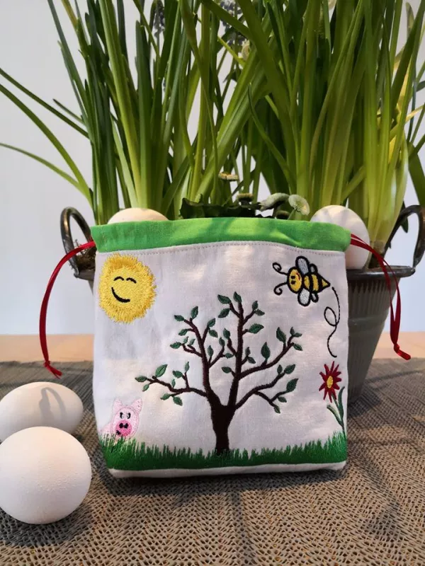 Stickdatei Set Frühlingswiese (div. Rahmengrößen), Foto zeigt hellen Stoffbeutel mit Kordelzugrand. Bunte Bestickung mit Wiese, Blume, Sonne, Biene, Schweinchen, Baum.