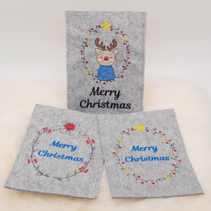 Stickdatei Set ITH Christmas-Cards - Grußkartenhüllen, Foto zeigt 3 Hochkant-Karten aus hellgrauem Filz. Bunte Bestickung mit jeweils diversem Kranz, darin Motiv Elch, bzw. Schriftzug "Merry Christmas".