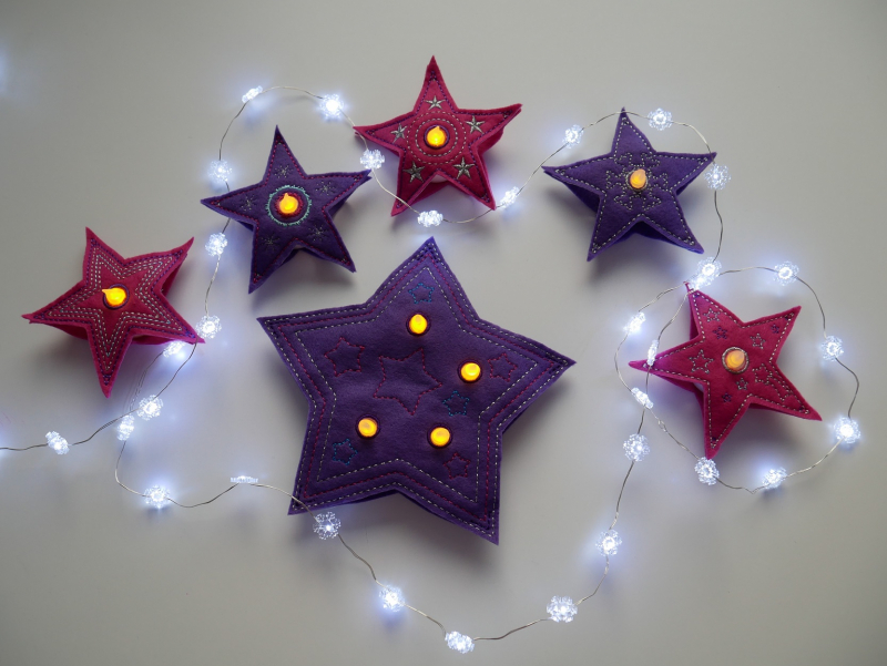 Stickdatei Set Christmas Lights (div. Rahmengrößen), Foto zeigt als LED-Cover in Sternformat 5 kleine und 1 großen Stern mit Öffnungen für Licht. Roter oder lila Filz, filigran bestickt. Die kleinen Sterne mit je einem LED-Platz, der große mit 4.