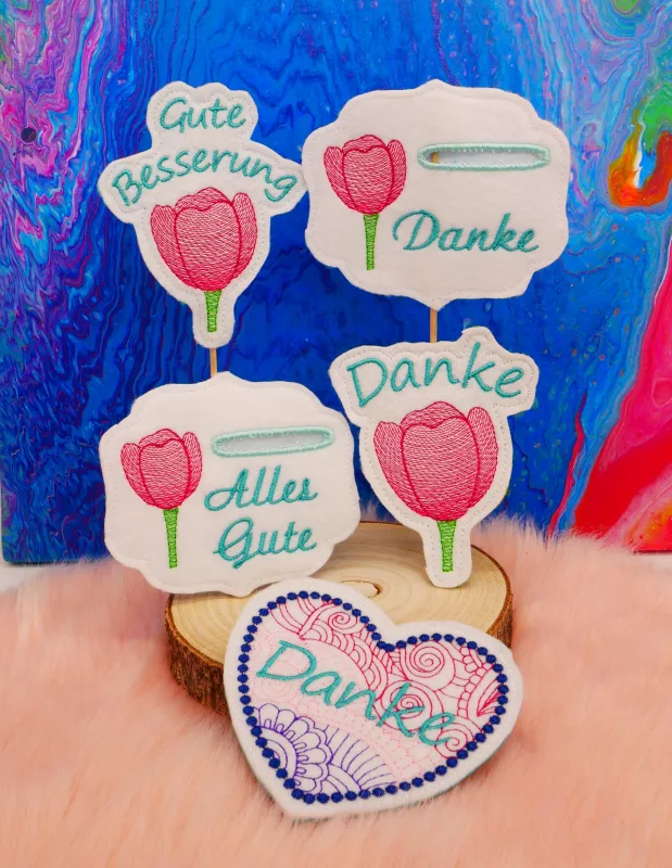 Stickdatei Set Danke & Genesung-Stabdesigns, Foto zeigt 5 Ausfertigungen. 1 einzelnes liegendes Herz mit Tupfenkranz, Innenbestickung rosa-rot-lila, türkiser Schriftzug "Danke". 4 helle Designstäbe, je mit rosa Tulpe und grünem Schriftzug "Danke", bzw. "A Stickdatei Set Danke & Genesung-Stabdesigns, Foto zeigt 5 Ausfertigungen. 1 einzelnes liegendes Herz mit Tupfenkranz, Innenbestickung rosa-rot-lila, türkiser Schriftzug "Danke". 4 helle Designstäbe, je mit rosa Tulpe und grünem Schriftzug "Danke", bzw. "A