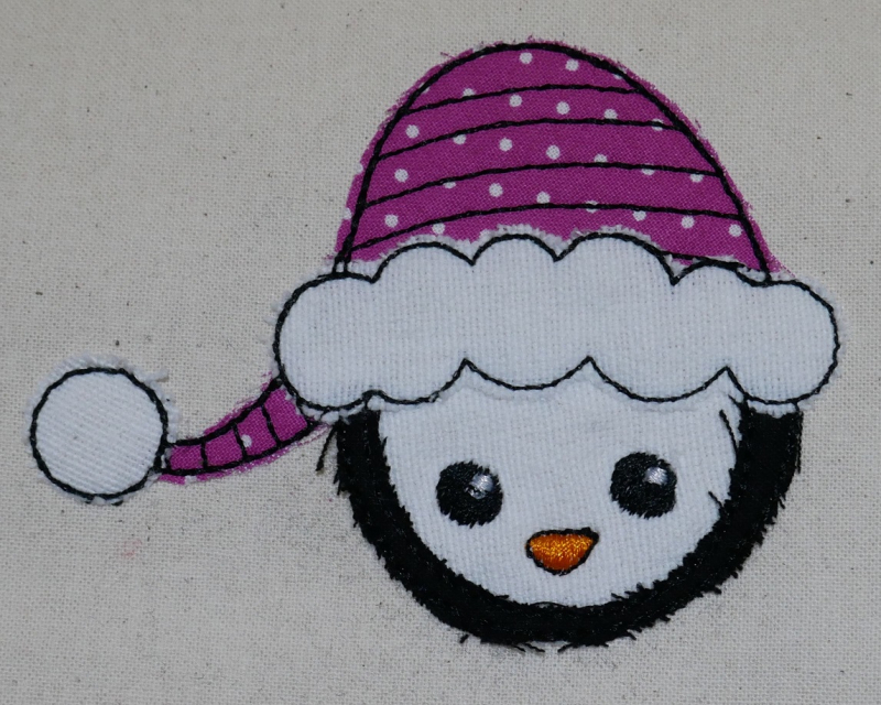 Stickdatei Set Christmas Faces Doodle-Applikationen, Foto von Applikation Schneemannkopf mit Mütze, aufgebracht auf hellen Stoff.
