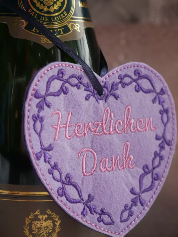 Freebie Danke Herzchen mit ITH Geschenkanhängern (10x10 und 13x18 Rahmen), Foto mit Herzform-Anhänger am dunklen Bändchen. Untergrund helllila Filz mit dunkellila Schnörkelrand und rosa Schriftzug "Herzlichen Dank".