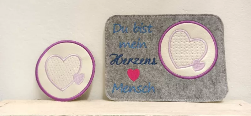 Freebie Stickdatei ITH Mug Rug Du bist mein Herzensmensch (10x10 und 13x18), Foto eines rechts im Bild befindlichen querformatigen Tassenteppichs aus mittelgrauem Filz. Blaufarbig bestickt mit dem Schriftzug "Du bist mein Herzensmensch" und rotem Herz. Kr