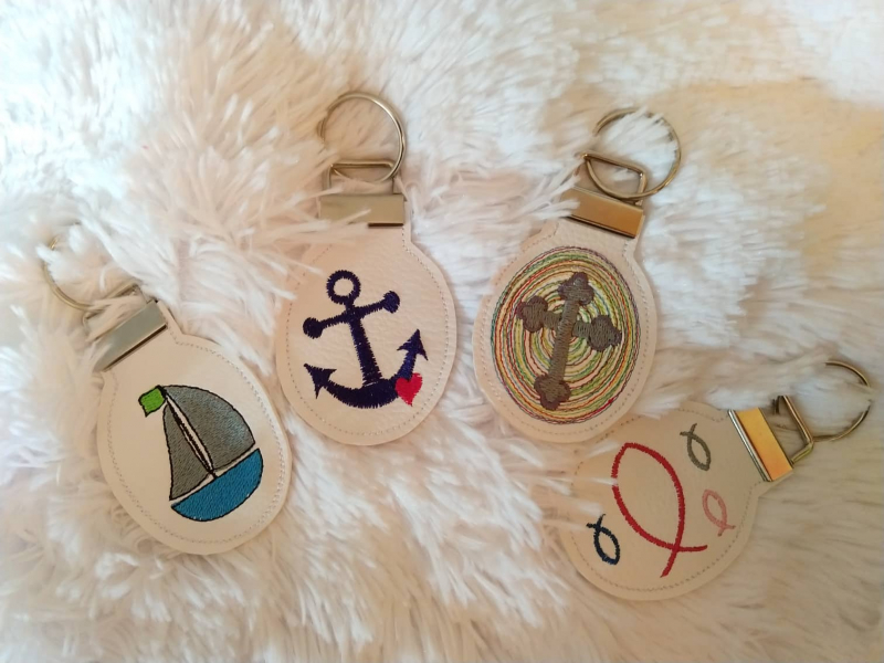 Stickdatei Set christliche Deko und Gastgeschenke (ITH), Foto zeigt 4 runde Anhänger. Diese mit angeklammerter Metallöse mit Schlüsselring und diversen Symbolen (Segelboot, Fische, Anker, Kreuz).