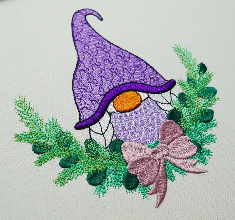 Christmas Gnome mit lila Mütze und Flechtzöpfen. Drumherum ist ein Zweig mit Schleife zu sehen.