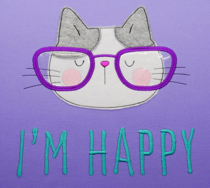 Stickdatei Spar-Set Cat Doodle Applikationen inkl. ITH Anhänger, Applikation Katzenkopf auf violettem Stoff. Beige-graue Katze mit lila Brille. Schriftzug "I´m happy" in türkis.