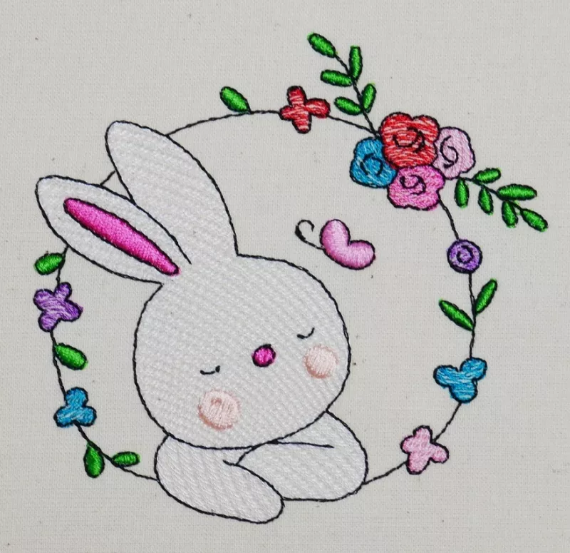 Osterhase mit floralem Kranz ausgestickt auf Baumwolle.