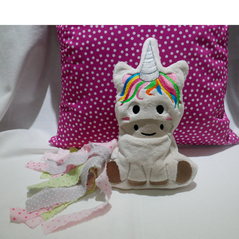 Stickdatei Sweet Unicorn (div. Rahmengrößen). Foto zeigt helles sitzendes Plüschtier-Einhorn mit bunter aufgestickter Mähne und Schweif aus diversen bunt bedruckten Stoffstreifen.