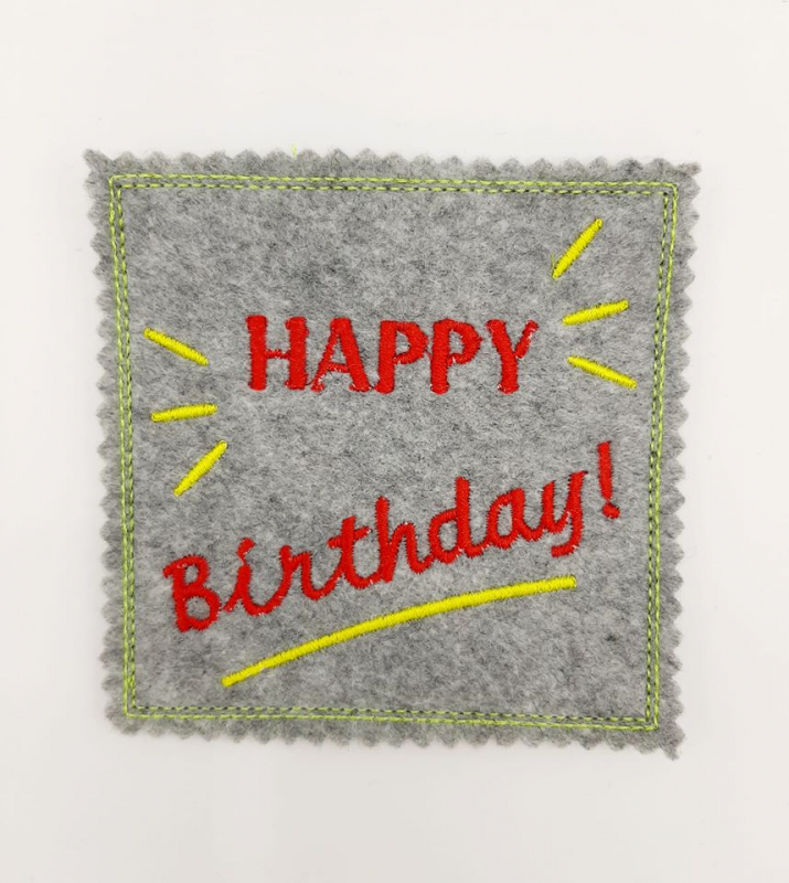 Stickdatei Set ITH Geburtstagskarten (10x10 u. 13x18), Foto zeigt quadratische Karte aus grauem Filz. Bestickung: Roter Schriftzug "HAPPY Birthday!" mit Strahlen/Strich in gelb.