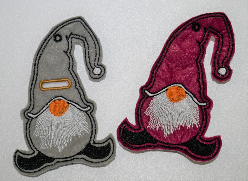 Stickdatei Set ITH Gnom Bestecktaschen und Geschenkanhänger (div. Rahmengrößen), Foto zeigt 2 Gnome mit Garn-Öse in der Zipfelmütze, einer zusätzlich mit Einstecköffnung. Der eine vorwiegend grau gehalten, der andere vorwiegend dunkelrot.