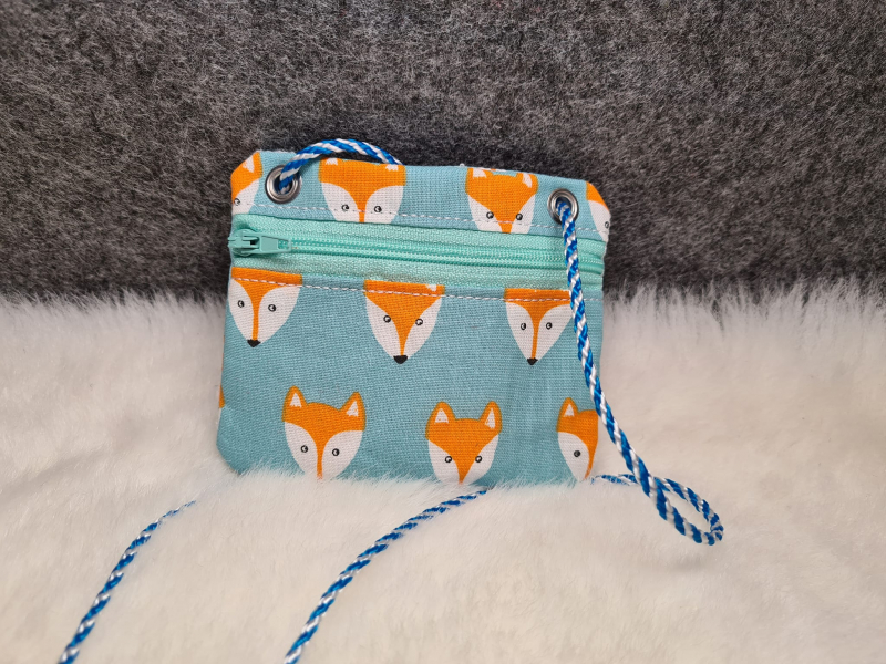 Stickdatei Set BLANKO ITH Taschen im Querformat mit türkisem Reißverschluss in der Front oben, darüber links und rechts je 1 Öse. Foto zeigt Design in türkisblauem Stoff, bedruckt mit Fuchsköpfen in orange/weiß/schwarz. Platziert auf hellem Fell, Hintergr Stickdatei Set BLANKO ITH Taschen im Querformat mit türkisem Reißverschluss in der Front oben, darüber links und rechts je 1 Öse. Foto zeigt Design in türkisblauem Stoff, bedruckt mit Fuchsköpfen in orange/weiß/schwarz. Platziert auf hellem Fell, Hintergr