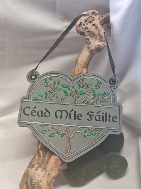 Stickdatei Set Monogramm Motiv Baum inkl. ITH Schild, Foto mit Ausfertigung, oberer Rand links und rechts geöst, mit Schnur, welche an Aststück hängt. Herzform mit Baum, vor dem der Schriftzug "Céad Mile Fáilte" quer vor diesem die Baumteile dieses Bereic Stickdatei Set Monogramm Motiv Baum inkl. ITH Schild, Foto mit Ausfertigung, oberer Rand links und rechts geöst, mit Schnur, welche an Aststück hängt. Herzform mit Baum, vor dem der Schriftzug "Céad Mile Fáilte" quer vor diesem die Baumteile dieses Bereic