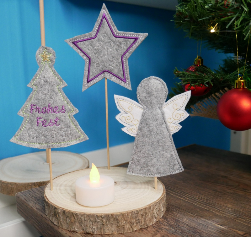 Stickdatei Set ITH Stabdateien mit Engel, Stern und Christbaum, Foto mit 3 Engeln in Designstäben, in Holzscheiben steckend. Grundlage immer grauer Filz. Motive: Engel mit weißen Flügeln; Tannenbaum mit Aufschrift "Frohes Fest"; Stern mit lila Kontrastumr Stickdatei Set ITH Stabdateien mit Engel, Stern und Christbaum, Foto mit 3 Engeln in Designstäben, in Holzscheiben steckend. Grundlage immer grauer Filz. Motive: Engel mit weißen Flügeln; Tannenbaum mit Aufschrift "Frohes Fest"; Stern mit lila Kontrastumr