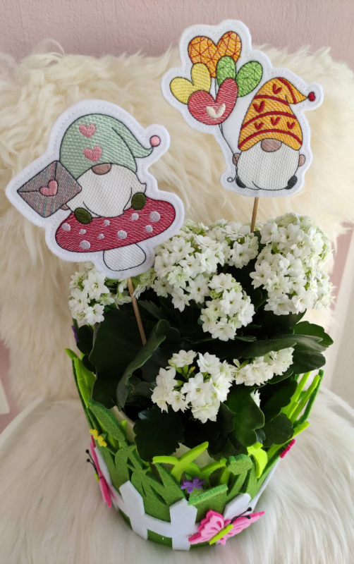 Stickdatei Set Lovegnomes ITH Stabdesigns, Foto zeigt Blumentopf mit Blütenpflanze und 2 bunten Designstäben. 1 mal Gnom auf Fliegenpilz mit Liebesbrief in der Hand; 1 mal Gnom mit Herzluftballons.