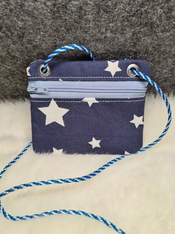 Stickdatei Set BLANKO ITH Taschen, Foto zeigt Querformat mit hellblauem Reißverschluss frontal an der Oberseite, platziert auf weißem Fell, Hintergrund grau. Außenstoff dunkelblau, mit unterschiedlich großen weißen Sternen bedruckt. Links und rechts oben