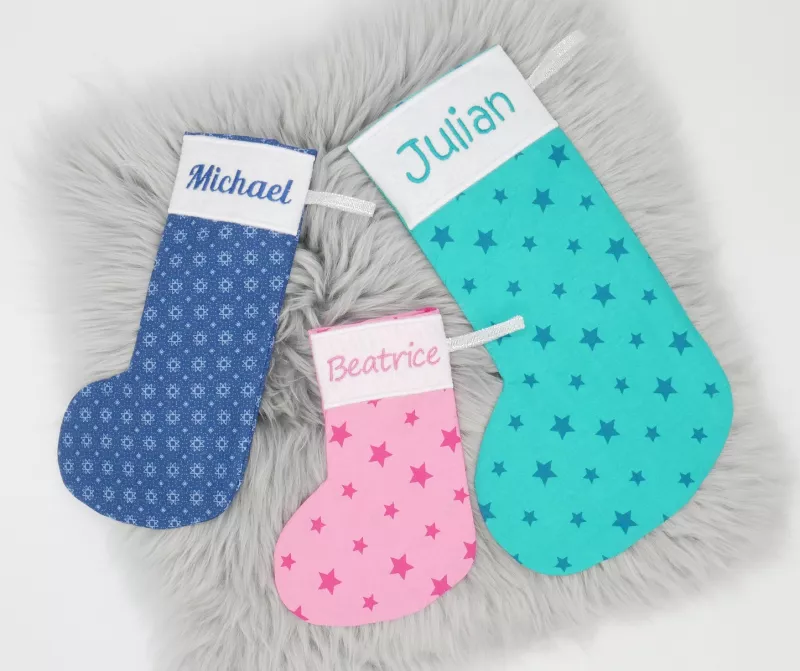 Stickdatei Set ITH Blanko Stiefel in vielen Größen + Schneeflockenanhänger, Foto zeigt 3 Stiefel unterschiedlicher Größen. Jeweils unterschiedliche bedruckte Stoffe, oben weißer Rand mit Schriftzug "Julian", "Beatrice", "Michael".