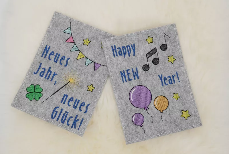 Stickdatei Set Gnom Silvesterparty mit ITH Kartenhüllen & Einzelmotive, Foto zeigt 2 Hochkant-Karten aus hellgrauem Filz. Eine mit Sternen, Girlande, Glücksklee, Wunderkerze, Aufschrift "Neues Jahr, neues Glück!"; eine mit Luftballons, Musiknoten, Sternen