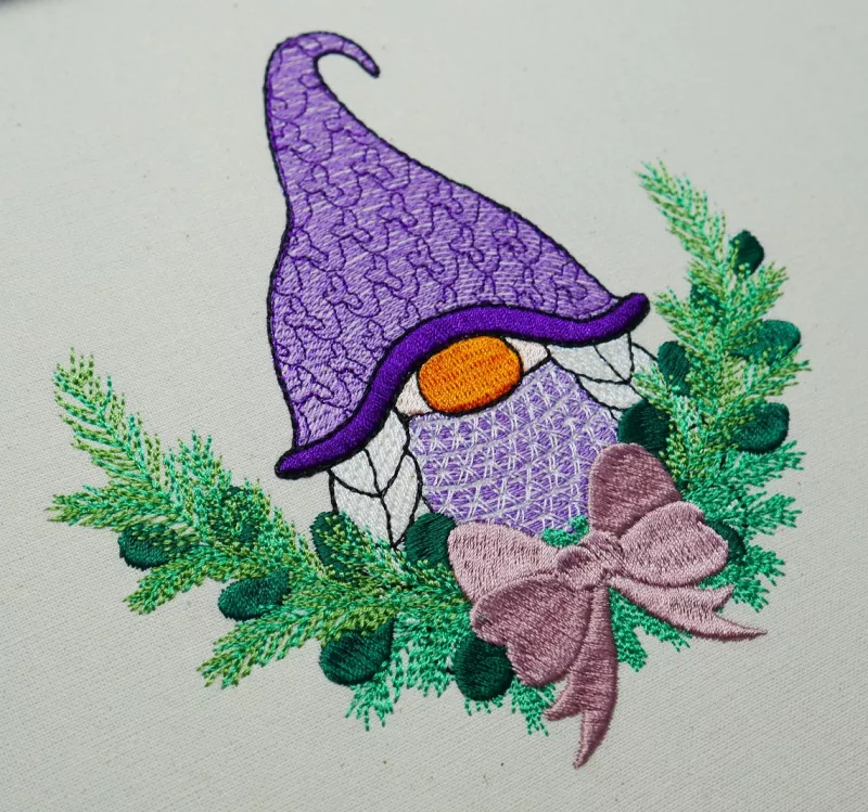 Christmas Gnome mit lila Mütze und Flechtzöpfen. Drumherum ist ein Zweig mit Schleife zu sehen.