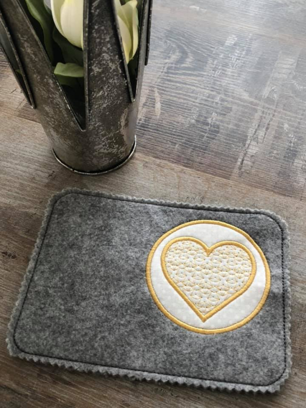 Stickdatei Set ITH Mug Rugs und Anhänger, Foto zeigt rechteckigen Tassenteppich aus dunkelgrauem Filz. Rechts oben kreisrunder Abstellplatz mit Herz darin in weiß-gelb. Herz zusätzlich mit Musterbestickung selbiger Farbtöne. Stickdatei Set ITH Mug Rugs und Anhänger, Foto zeigt rechteckigen Tassenteppich aus dunkelgrauem Filz. Rechts oben kreisrunder Abstellplatz mit Herz darin in weiß-gelb. Herz zusätzlich mit Musterbestickung selbiger Farbtöne.