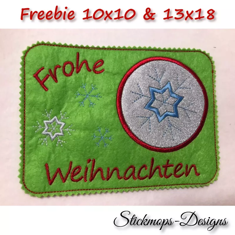 Freebie Stickdatei ITH Mug Rug Frohe Weihnachten (10x10 und 13x18), Foto mit Ausfertigung  auf grünem querformatigem Filz. Schriftzug "Frohe Weihnachten" und Umrandung Abstellplatz in rot. Abstellplatz innen silberfarben mit Eiskristallbestickung in blau,