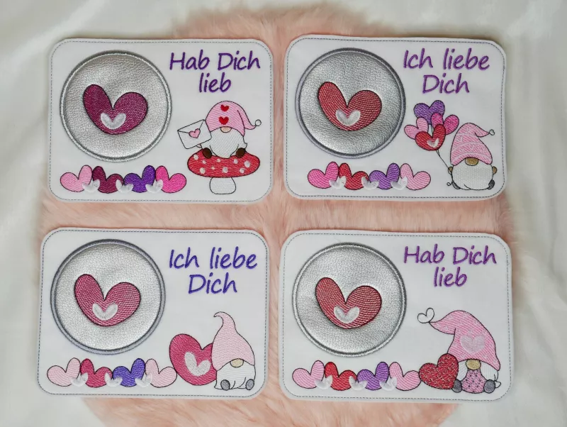 Stickdatei Set Lovegnomes Sparset 4 in 1 mit Dateien für Mugrugs, Schokohüllen, Anhänger und Stabdesigns, Foto zeigt 4 querformatige Tassenteppiche, auf apricotfarbenem Fell präsentiert. 4 unterschiedliche Gnommotive (Gnom auf Fliegenpilz mit Brief; Gnom