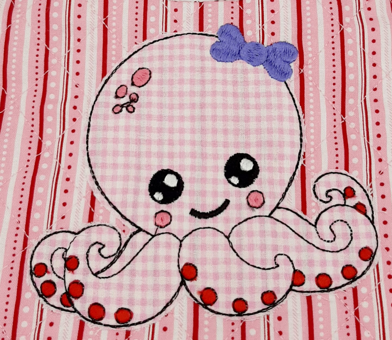 Stickdatei Set Octopus Applikation für Junge & Mädchen, Foto zeigt bestickte Oktopus-Applikation aus rosa-weiß kariertem Stoff auf linear gemustertem Stoffuntergrund. Dicke Stickschleife am Kopf.