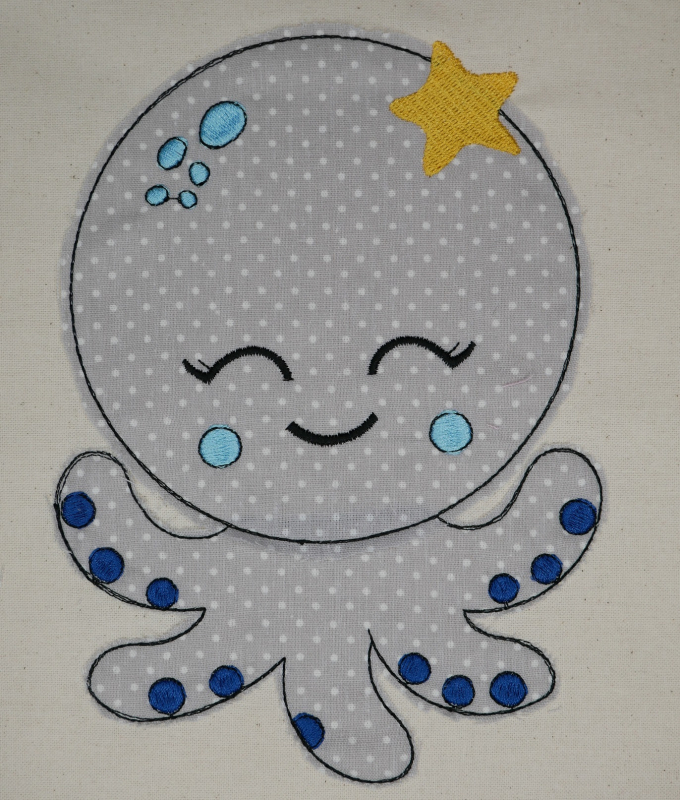 Stickdatei Set Octopus Applikation für Junge & Mädchen, Foto zeigt bestickte Oktopus-Applikation aus grau-weißem Stoff auf hellem Stoffuntergrund. Stern am Kopf.