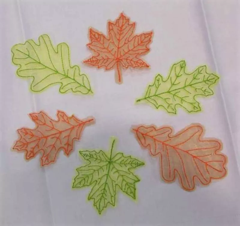 Stickdatei Set Herbstblätter inkl. ITH Anhänger, Foto mit 6 Blättern auf hellem Untergrund. Gestielte Blätter aus Organza, in orange oder grün, aufgestickte Blattaderstruktur.