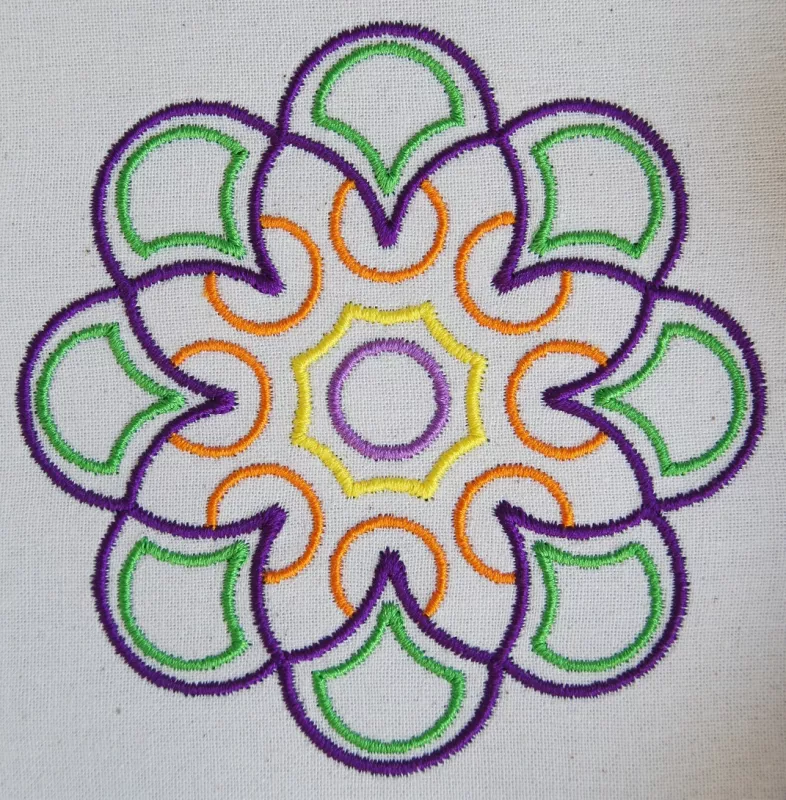 Stickdatei-Set Ornamente Dream 10 x 10 cm, Foto mit bogenartigem Blütenornament in eher grober Ausfertigung auf hellem Stoff. Lila, grün, orange, pink, gelb.