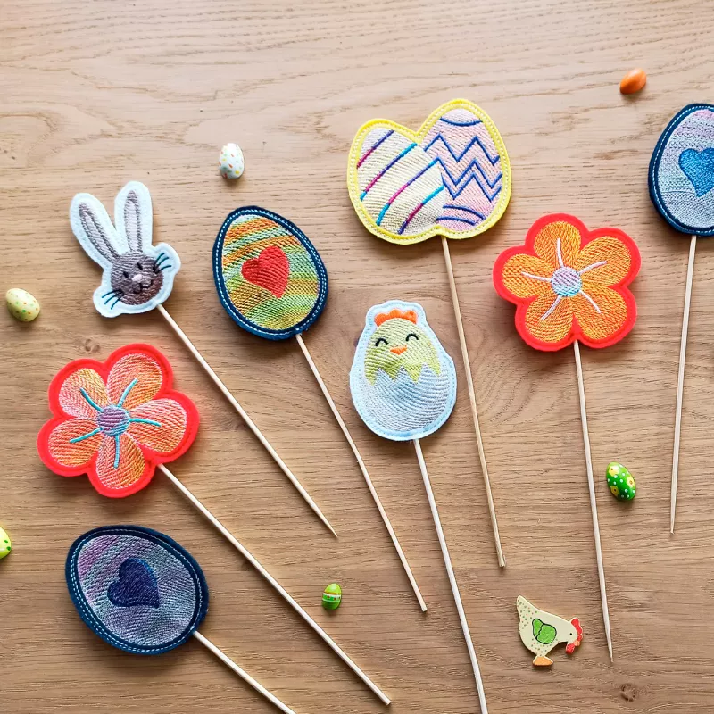 Ausgestickte Stabdeko mit Hase, Blume, Ei und Küken.