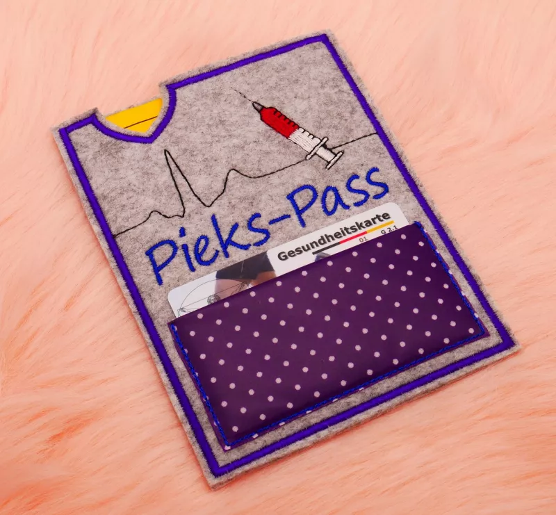 Stickdatei Set ITH Impfpass-Hüllen 24 Designs (13x18), Foto mit Hülle aus grauem Filz auf orangem Felluntergrund. Bestickung: EKG-Kurve mit Spritze und Schriftzug "Pieks-Pass", Einsteckapplikation aus gepunktetem Stoff mit Krankenkassenkarte darin.