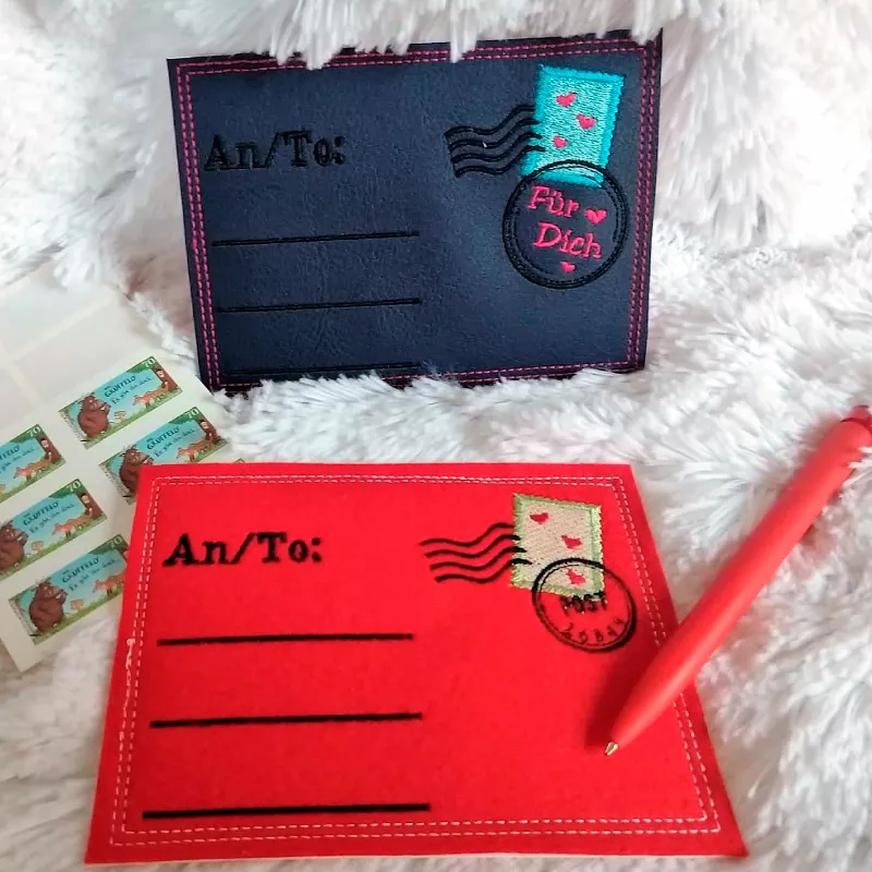 Stickdatei Set ITH Postkarten inkl. Abwandlung zur Geschenktasche (div. Größen), Foto zeigt 2 Karten, eine dunkelblaue, eine rote. Beide links bestickt "An/To", darunter 3 Linien. Rechts gestickte Briefmarke mit 2 Stempeln, einmal mit Schriftzug "Post" da