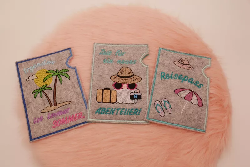 Stickdatei Set ITH Reisepasshüllen (13x18) + Einzelmotive, Foto zeigt 3 hellgraue Filzhüllen in Hochkant-Format. Bunte Bestickung mit Urlaubsmotiven und Schriftzügen ("Reisepass", "Irgendwo ist immer Sommer", "Zeit für ein neues Abenteuer").