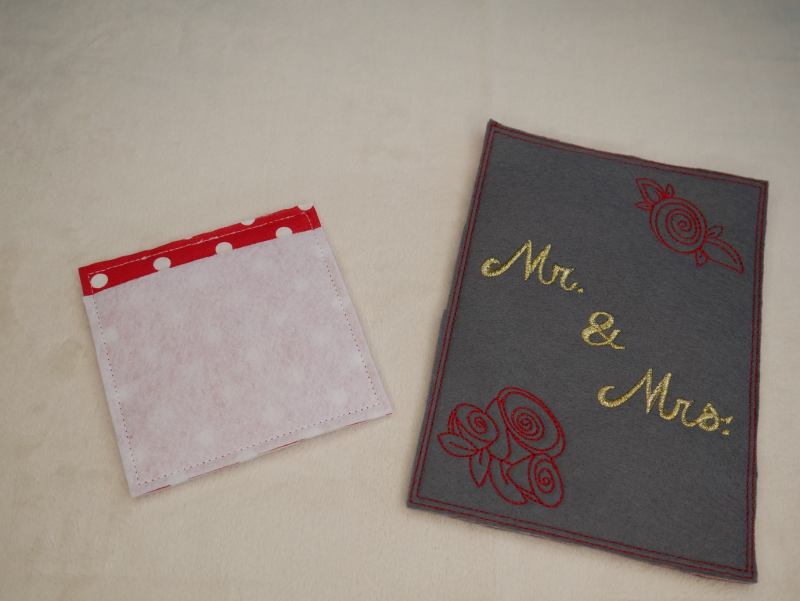 Stickdatei Set Hochzeit, Foto zeigt rechts eine Karte aus dunklem Filz. Hochkant, Bestickung in rot und gelb: Rosenköpfe, Schriftzug "Mr. & Mrs.". Linksseitig die Rückseite einer quadratischen Geschenktasche, die zeigt, dass man die Karte auch auf diese W