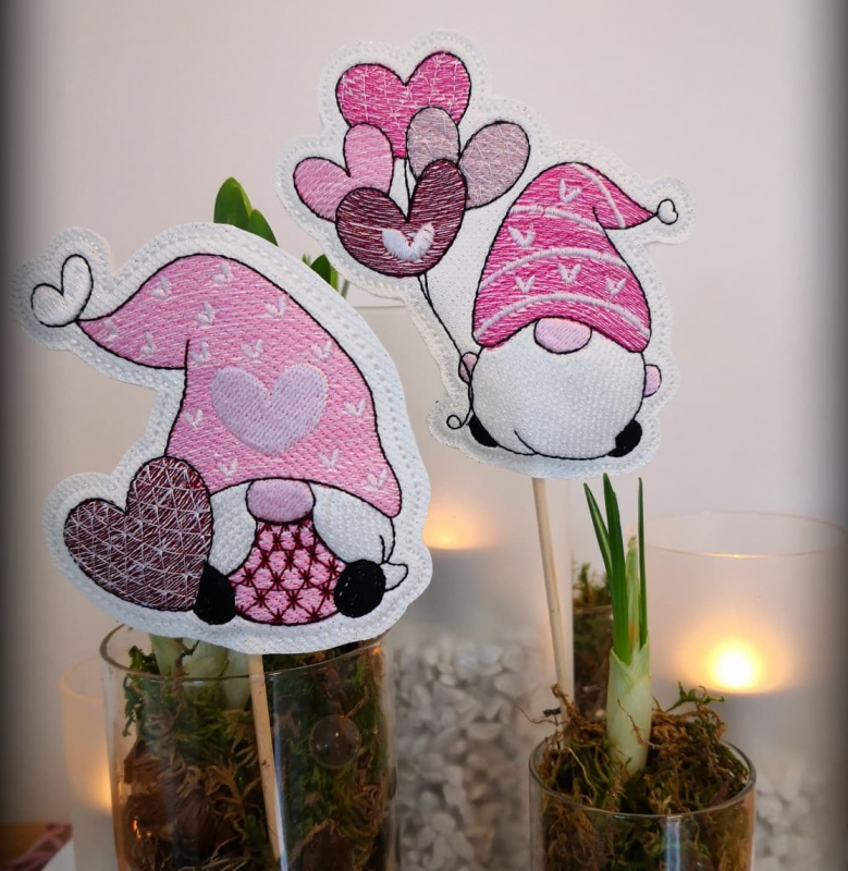 Stickdatei Set Lovegnomes ITH Stabdesigns, Foto zeigt 2 Designstäbe, beide in rosa-rot-lila-Tönen gehalten, auf weißem Untergrund. 1 mal Gnom mit Herz; 1 mal Gnom mit Herzluftballons.