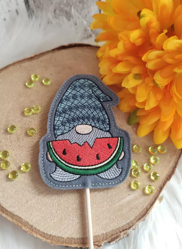 Stickdatei Set ITH Stabgnome 4 Jahreszeiten (10x10). Foto zeigt Designstab mit Gnom in grau-blau, der ein Stück angebissene Wassermelone in den typischen Farben hält.