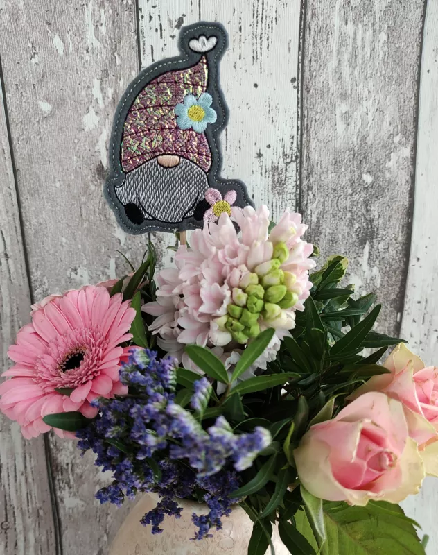 Stickdatei Set ITH Stabgnome 4 Jahreszeiten (10x10), Foto zeigt Designstab in Blumenvase mit Blumen steckend. Gnom mit farbiger Mütze und gelb-türkiser Blüte daran.