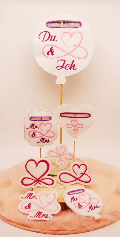 Stickdatei Set Liebe & Hochzeit - Stabdesigns, Foto mit 8 Designs, präsentiert auf Holzscheibe, die auf orangem Fell liegt. Ohne Einstecköse: 4 mal unterschiedliches Schnörkel-Herz, eins davon mit Schriftzug "Mr. & Mrs.". Mit Einstecköse: 2 mal Luftballon