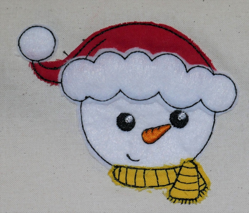 Stickdatei Set Christmas Faces Doodle-Applikationen, Foto zeigt auf hellen Stoff aufgebrachte Applikation. Schneemannkopf mit Mütze und Schal.