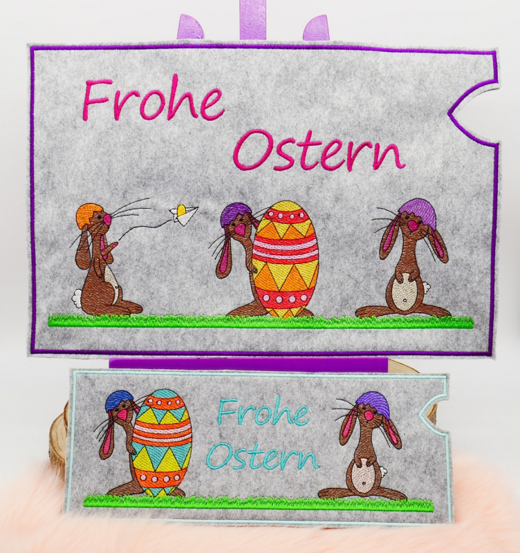 Stickdatei Set Hase Jasper ITH Geschenk- und Schokoladenhüllen inkl. Stabdeko, Foto zeigt 2 hellgraue querformatige Filzhüllen, bunt bestickt. Beide mit Schriftzug "Frohe Ostern". Größere mit unterschiedlichen 3 Hasen und Osterei, kleinere mit unterschied