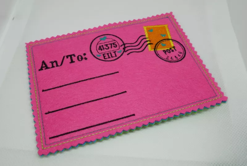 Stickdatei Set ITH Postkarten inkl. Abwandlung zur Geschenktasche (div. Größen), Foto zeigt 1 Karten in pink. Links bestickt mit "An/To:", darunter 3 Linien Für Adresse. Rechts gestickte Briefmarke mit 3 Stempeln, 2 mit Postleitzahlen, Schriftzug "EILT" u