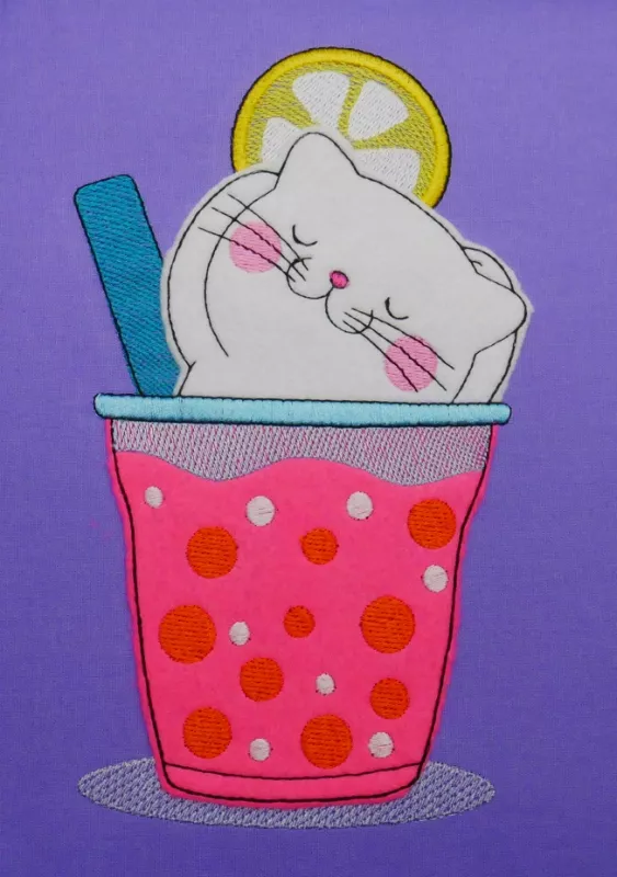Stickdatei Set Hello Summer Cat Doodle Applikation inkl. ITH Anhänger, Foto zeigt Applikation auf lila Stoff. Katze, beigefarben im Glas mit Zitronenscheibe und grünem Strohhalm, badend in rosarotem Drink.