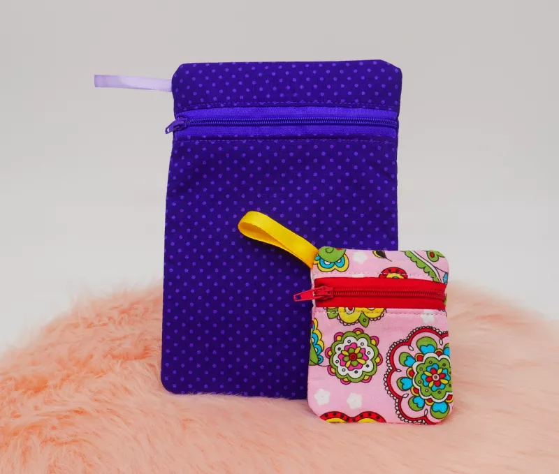 Stickdatei Set BLANKO ITH Taschen im Hochformat mit Reißverschluss (obere Vorderseite) und Stoffschlaufe, über 60 Größen, Foto mit einer großen und einer kleinen Tasche voreinander, auf orangefarbenem Fell platziert. Große Tasche in lila, rosa gepunktet,