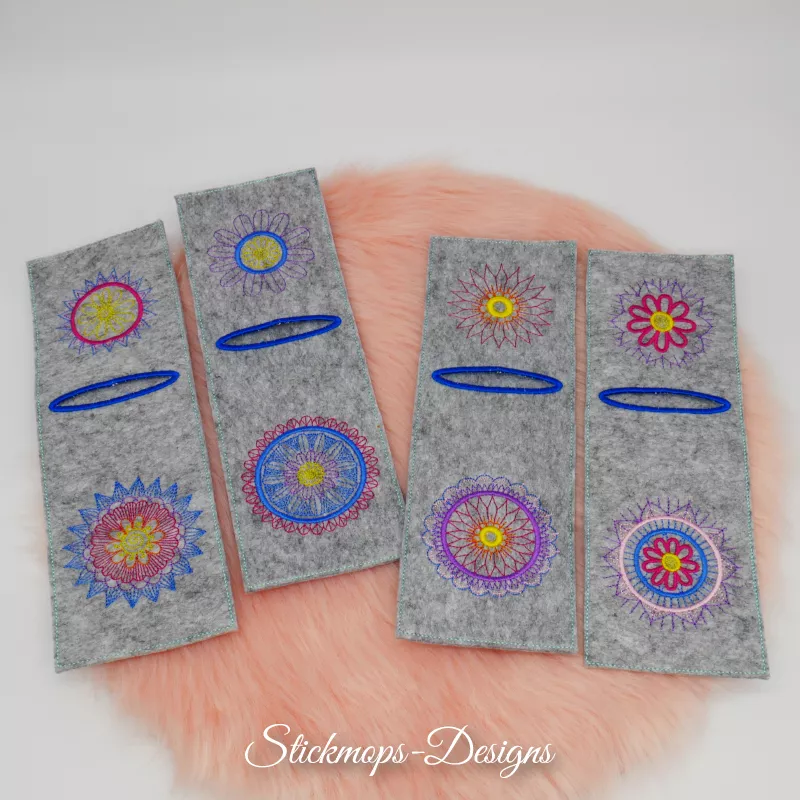 Stickdatei Set Mandala-Bestecktaschen + Einzelmotive, Foto mit 4 mittelgrauen Filztaschen, auf orangefarbenem Fell liegend. Jede mit blau umstickter Öffnung im oberen Drittel und jeweils unterschiedlichen Bestickungen oberhalb und unterhalb davon.