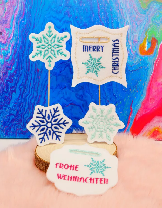 Stickdatei Set Weihnachts-Stabdesigns, Foto mit 5 Designs vor buntem Hintergrund auf Holzscheibe mit orangem Fell darunter. 3 mal unterschiedliche Eiskristalle (blau, grün bzw. türkis). 2 mal mit Einstecköffnung, Eiskristallbestickung, rahmenartiges, bzw. Stickdatei Set Weihnachts-Stabdesigns, Foto mit 5 Designs vor buntem Hintergrund auf Holzscheibe mit orangem Fell darunter. 3 mal unterschiedliche Eiskristalle (blau, grün bzw. türkis). 2 mal mit Einstecköffnung, Eiskristallbestickung, rahmenartiges, bzw.